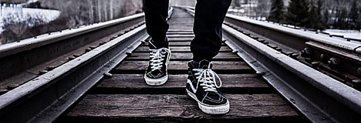 A person with black and white shoes standing on train tracks.